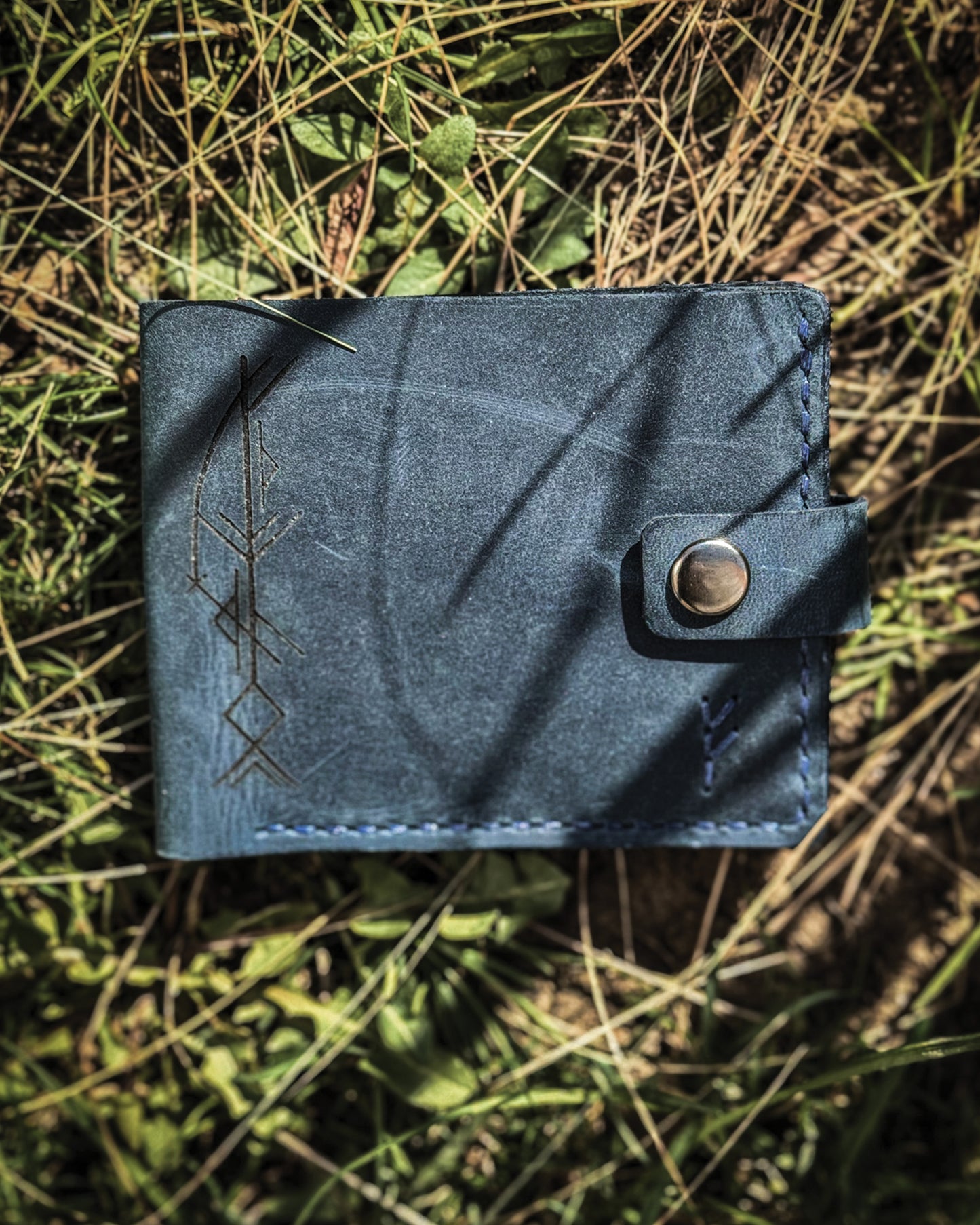 Handmade Viking leather wallets engraved with a custom Bindrune for wealth, prosperity & luck. Features stitched Fehu rune. Available in navy, black & green. Norse mythology meets everyday style.