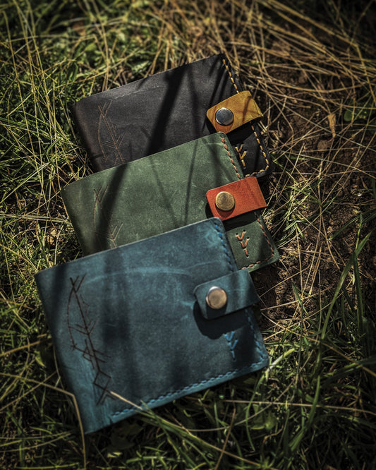 Handmade Viking leather wallets engraved with a custom Bindrune for wealth, prosperity & luck. Features stitched Fehu rune. Available in navy, black & green. Norse mythology meets everyday style.