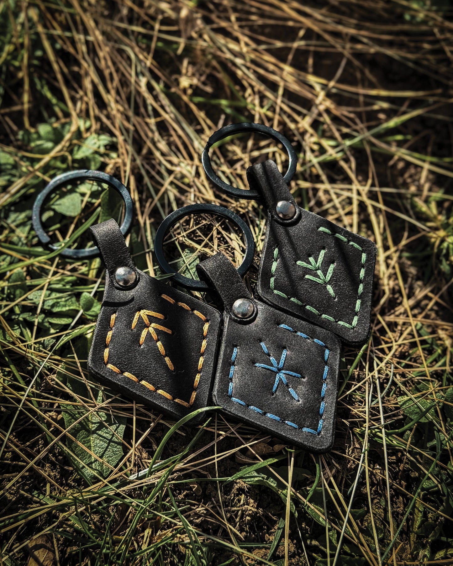 Three handmade black leather Viking keychains featuring rune symbols for protection, victory, and hospitality—stitched in green, tan, and blue for powerful Norse symbolism.