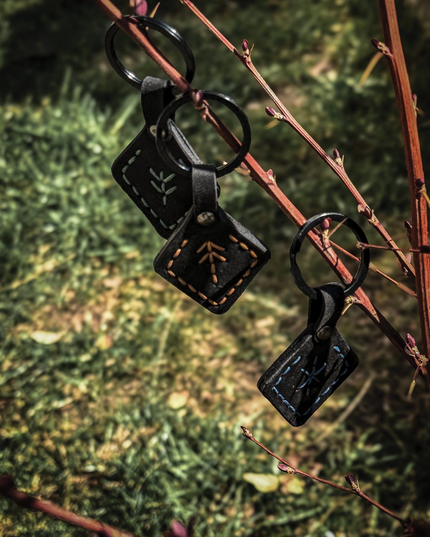Three handmade black leather Viking keychains featuring rune symbols for protection, victory, and hospitality—stitched in green, tan, and blue for powerful Norse symbolism.