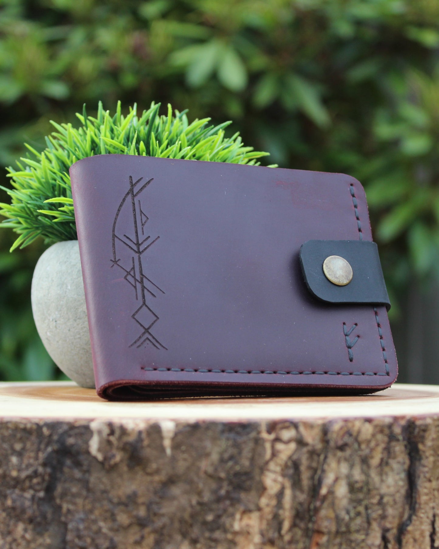 Dark Red leather wallet with engraved design on a wooden stump with greenery in the background